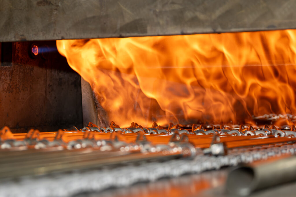 Image of parts on a conveyor belt heading towards a burning brazing furnace.